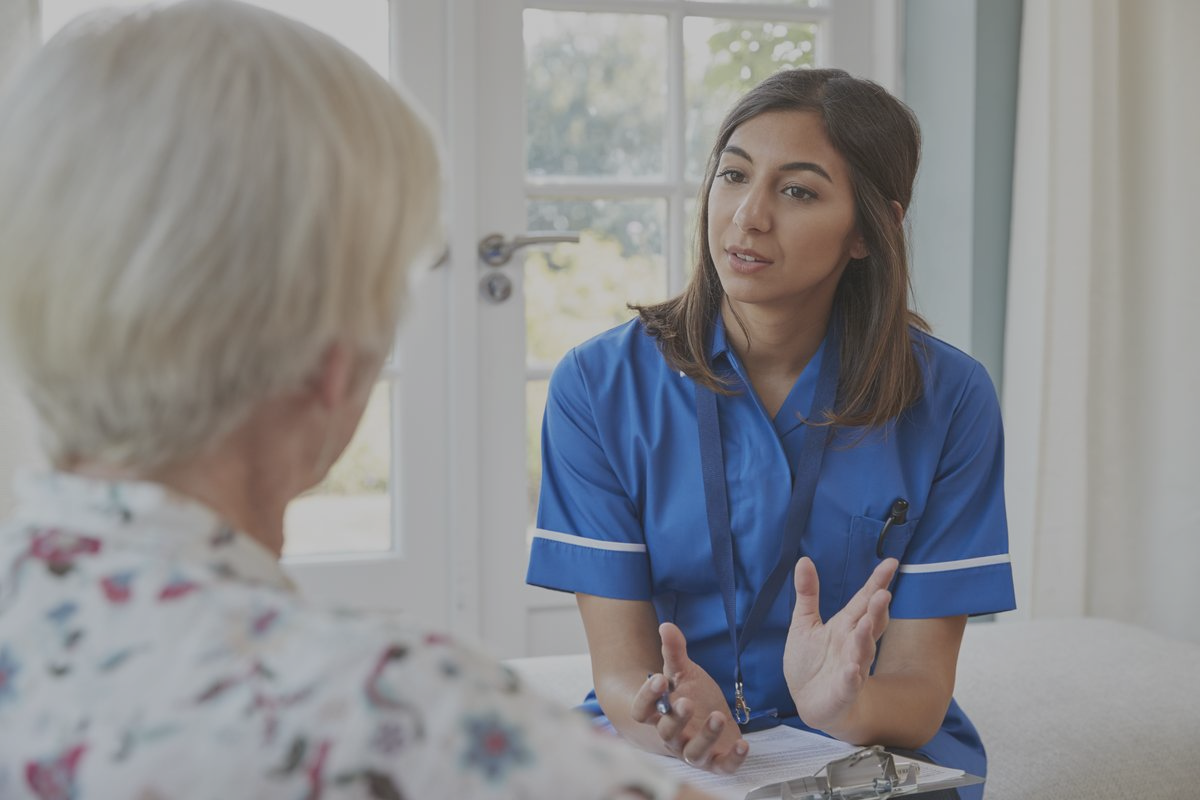 Young nurse in blue scrubs talking to elderly woman