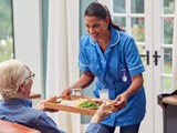 Female Care Worker In Uniform Bringing Meal On Tray